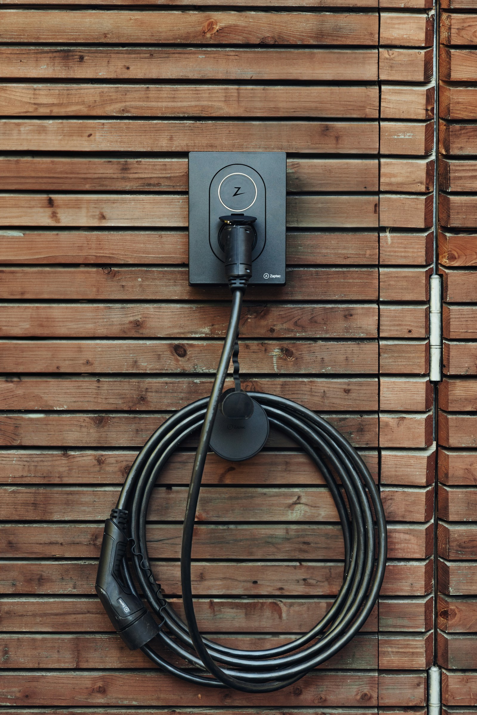 Level 2 EV charger with the charging cable coiled neatly on a wood-sided wall