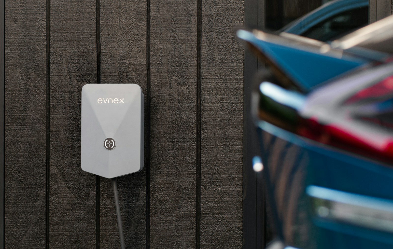 Wall-mounted Level 2 EV charger on the side of a home with a car parked alongside